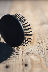 Black hairbrush with blonde hair on wooden floor.