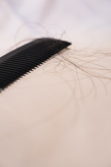 Close-up of black comb with brown hairs on bright fabric.