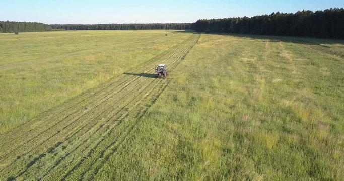 impressive panoramic view tractor with mower cuts grass for hay driving along field with trees reflection