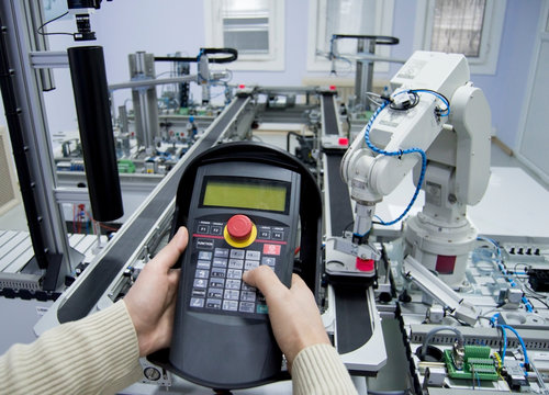 Man is pushing button on teach panel to control a robotic arm which is integrated on smart factory production line. industry 4.0 automation line which is equipped with sensors and robotic arm.
