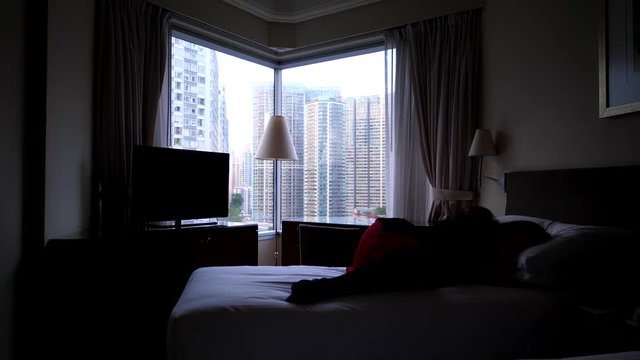 Depressed woman lie on bed, dark room. Lady in red skirt and black suit lie over blanked, feel down and exhausted. Bright city seen outdoors through corner window