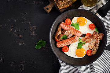 English breakfast - fried egg, tomatoes, sausage and bacon. Top view