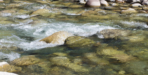 Water in the mountain raging river. Beautiful natural background of stones and water. Texture of clear water and fast river. Backdrop with copy space