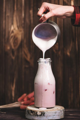 Woman hand pouring milkshake in bottle on wooden background