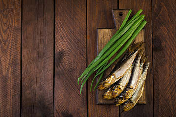 Smoked sprat and green onion  on a cutting board on a wooden background. Smoked fish. Top view