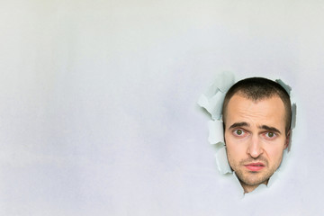 Sad man making hole in paper, looking at the camera, the awkward moment,  dissatisfied, blue...