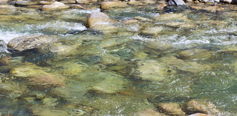 Water in the mountain raging river. Beautiful natural background of stones and water. Texture of clear water and fast river. Backdrop with copy space