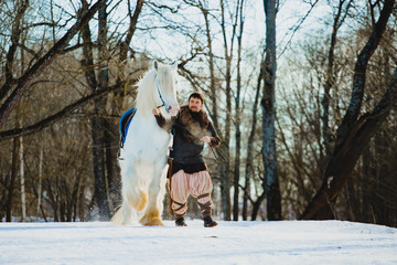 Fototapeta na wymiar Man in suit of ancient warrior walking with the big white horse