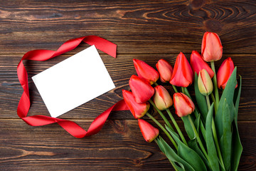 Red tulips with red ribbon and greeting card on dark wooden background. 
