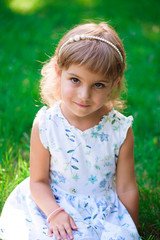 Portrait of a smiling little girl sitting on green grass.