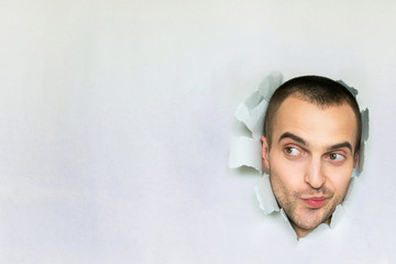 Funny man making hole in paper, playfully looking to the side,  surprise, pursed his lips,...