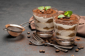 two portions Classic tiramisu dessert in a glass on dark concrete background