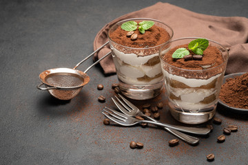 two portions Classic tiramisu dessert in a glass on dark concrete background