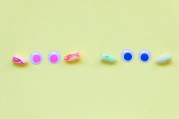 Two pairs of earplugs and eyes on the yellow background. Good sleep and noise protection concept.