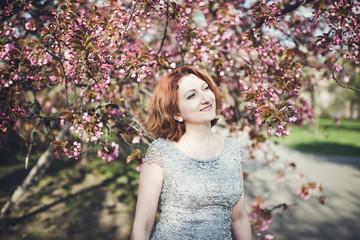 Cheerful middle aged Armenian woman in an elegant dress under the blooming sakura tree.