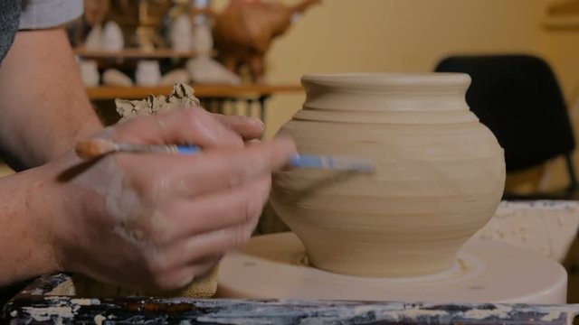 Professional male potter shaping pot with special tool in pottery workshop, studio. Crafting, artwork and handmade concept