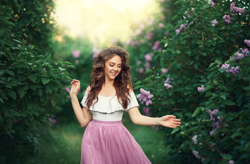 Outdoor fashion photo of beautiful young woman surrounded by lilac flowers garden. Spring blossom. 