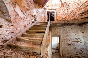 Large spacious forsaken empty basement room of ancient building or palace with cracked plastered brick walls, dirty floor and wooden staircase ladder.