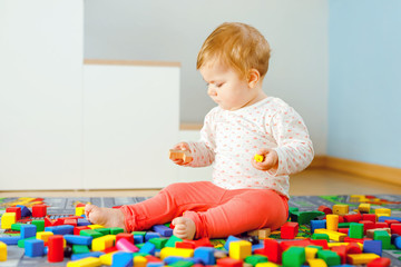 Adorable baby girl playing with educational toys . Happy healthy child having fun with colorful different wooden blocks at home in domestic room. Baby learning colors and forms