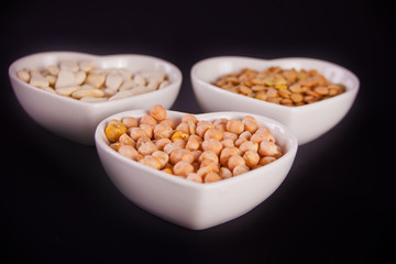 A plates of dry beans, peas and chickpeas on black background.