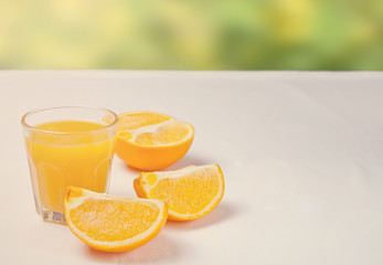 Glass of orange juice and slices of orange fruit on white table with nature on the background