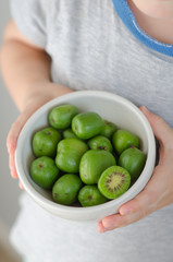 Mini kiwi in a plate in the hands of a child. Small exotic fruits on white background.