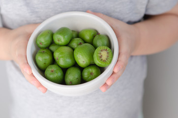 Mini kiwi in a plate in the hands of a child. Small exotic fruits on white background.