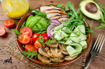 Healthy salad bowl with chicken, mushrooms, tomatoes, cucumbers, avocado and arugula