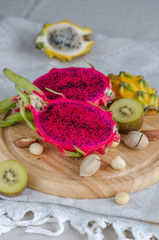 Assortment dragon fruit - yellow and red pitahaya, yellow kiwi and nuts on a wooden tray