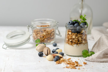 Healthy breakfast - glass jars of granola with fresh blueberries, yogurt, nuts and mint. Granola on a light background, space for text.