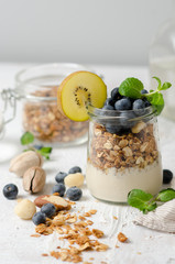 Healthy breakfast - glass jars of granola with fresh blueberries, yogurt, nuts and mint. Granola on a light background, space for text.