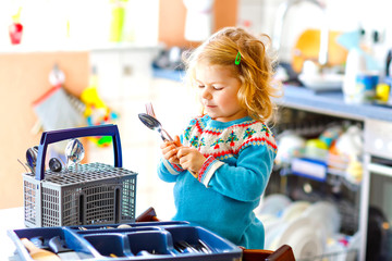 Cute little toddler girl helping in the kitchen with dish washing machine. Happy healthy blonde...