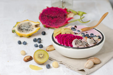 Obraz na płótnie Canvas Eating healthy breakfast bowl. Smoothie whith red and yellow dragon fruit , yellow kiwi and blueberries in white ceramic bowl.