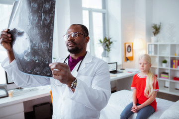 Dark-skinned doctor looking at the x-ray of cute schoolgirl