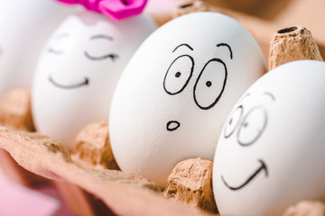 close up view of eggs with different face expressions in egg carton