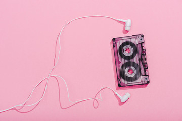 top view of vintage audio cassette with earphones on pink, music concept