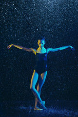 Young female ballet dancer performing under water drops and spray. Caucasian model dancing in neon lights. Attractive woman. Ballet and contemporary choreography concept. Creative art photo.