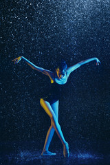 Obraz na płótnie Canvas Young female ballet dancer performing under water drops and spray. Caucasian model dancing in neon lights. Attractive woman. Ballet and contemporary choreography concept. Creative art photo.