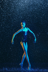 Young female ballet dancer performing under water drops and spray. Caucasian model dancing in neon lights. Attractive woman. Ballet and contemporary choreography concept. Creative art photo.