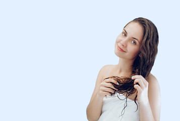 Beautiful young woman touching her wet  hair with hands and smiling while standing in front of the mirror  in bathroom. Hair  skin care concept