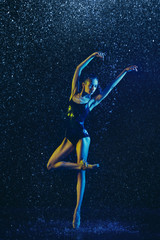Young female ballet dancer performing under water drops and spray. Caucasian model dancing in neon lights. Attractive woman. Ballet and contemporary choreography concept. Creative art photo.