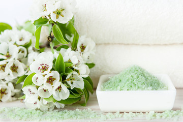 Obraz na płótnie Canvas Blossoming apple tree flowers, aromatic sea salt and towels. Concept for spa, beauty and health salons. Close up photo on white wooden background, selective focus
