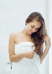 Naklejka premium Portrait Of Beautiful Young Female Model in Bath Applying Hair Oil. Closeup Of Sexy Woman In Towel Drying Wet Long Hair. Health And Beauty Concept. Protection moisturizing.