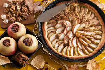 Apple pie and apples baked with cinnamon and jam surrounded by autumn leaves on a vintage wooden...