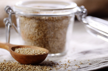 Raw organic superfood gluten free quinoa seeds in wooden spoon and glass airtight jar on kitchen table closeup