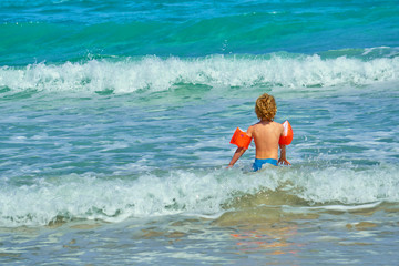 Blonde Child With Water Wings or Inflatable Rings In A Turquoise Sea