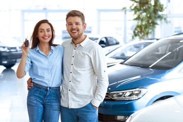 First big buy together. Portrait of a happy young couple hugging in a car salon showing car keys to a newly bought vehicle copyspace on the side