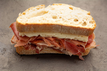 tasty Spanish ham and cheese on bread over dark background
