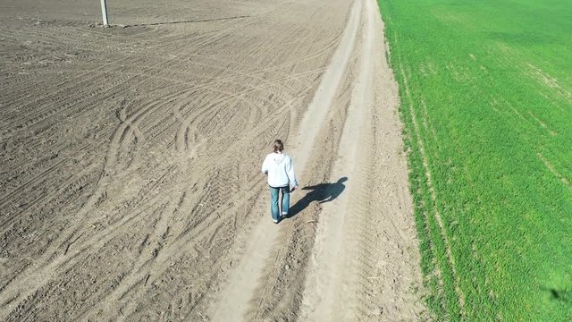 Aerial: Flying over Young man which walking footpath or dirt village rural country road on the early spring field.