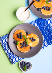 Pancakes served with fresh blueberries on gray plate over geometrical background. Healthy home made breakfast concept